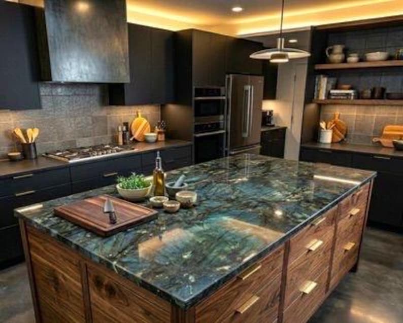 May include: A kitchen island with a polished blue and green labradorite stone countertop and a wooden base with gold handles. On the surface sits a wooden cutting board with a knife, a bowl of green herbs, a glass oil bottle, and small bowls.
