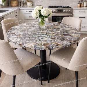 May include: A round dining table with a unique stone top featuring a mix of gray, white, and brown hues. The table is supported by a black pedestal base and surrounded by four beige upholstered chairs. A vase of white flowers sits in the center.