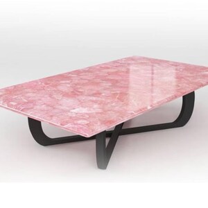 May include: A pink marble coffee table with a black, modern, X-shaped base.