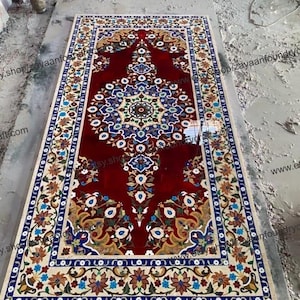 May include: A red, white, and blue floral patterned rug made of inlaid marble. The rug has a central medallion with a geometric design.