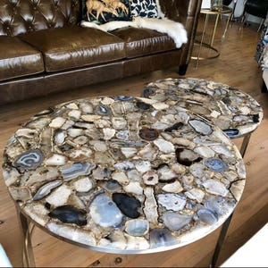 May include: Two round agate coffee tables with a natural stone top and a silver metal base. The tables are on a wooden floor.