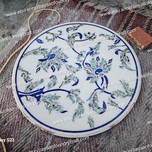May include: A white marble table top with a blue and green floral design inlaid with mother of pearl. The design features intricate details and a delicate floral pattern.