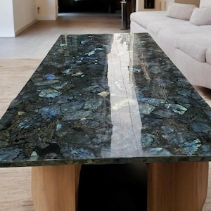 以下が含まれることがあります： 濃い青と緑のラブラドライトの石の天板と木製の脚を持つコーヒーテーブル。石はキラキラと光る効果があります。