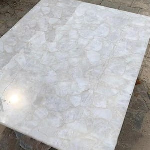 May include: A white quartz table top with a unique, natural, and textured surface. The table top is made of many small pieces of quartz that have been joined together to create a beautiful and unique design.