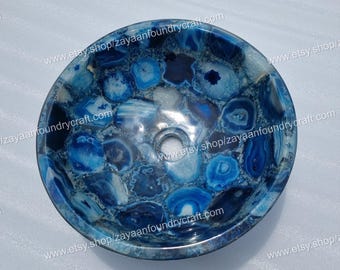 May include: A round, blue agate stone sink with a central drain hole. The sink features a mosaic pattern of various shades of blue and white, creating a unique and decorative design. The sink is a natural stone product.