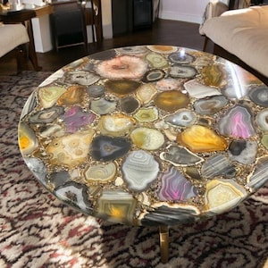 Könnte beinhalten: Ein runder Couchtisch mit einer einzigartigen Tischplatte aus Achat. Die Tischplatte besteht aus vielen verschiedenen Farben und Mustern von Achat, darunter Braun, Gold, Rosa und Lila. Der Tisch hat ein goldenes Metallgestell.