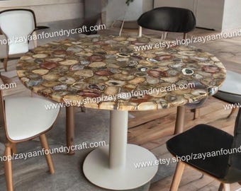 May include: A round dining table with a unique agate stone top. The table features a white pedestal base and is surrounded by several chairs. The agate top displays a variety of colors, including brown, beige, and red, creating a natural, decorative surface.