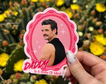 May include: A pink sticker with a portrait of a man with a mustache, wearing a black top, and the text "DADDY Is A State Of Mind". The sticker has a pink scalloped border and is set against a background of cacti and yellow flowers.