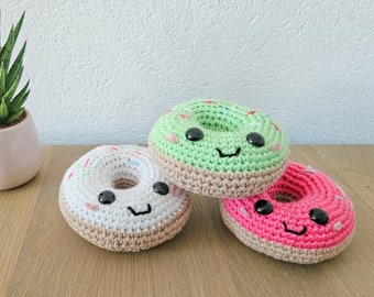 Puede incluir: Tres donuts de crochet con caras felices. Los donuts son verdes, blancos y rosas con chispas blancas.