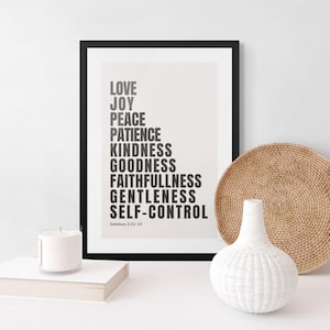 Może przedstawiać: Oprawiony wydruk z czarnym napisem "LOVE, JOY, PEACE, PATIENCE, KINDNESS, GOODNESS, FAITHFULLNESS, GENTLENESS, SELF-CONTROL". Widoczna jest również biała świeca, biały wazon i pleciony talerz.