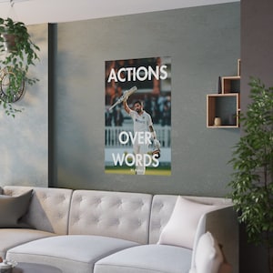 以下が含まれることがあります： クリケットの選手がバットを上げて喜びを表している、やる気を起こさせるポスター。ポスターには「ACTIONS OVER WORDS」というテキストと、選手の「KL Rahul」という名前が下に書かれている。