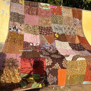 Könnte beinhalten: Ein Patchwork-Quilt aus verschiedenen Stoffen in Braun-, Rosa- und Orangetönen. Der Quilt besteht aus rechteckigen Teilen, die mit weißen Nähten zusammengenäht sind. Er ist über eine Wand drapiert.