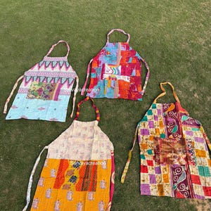 May include: Five colorful aprons with unique patchwork designs are displayed on green grass. Each apron features a different pattern, including floral, geometric, and abstract designs. The aprons have neck straps and waist ties.