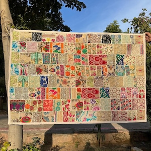 May include: A rectangular patchwork quilt with a cream border. The quilt features numerous fabric squares in various colours and patterns, including floral, paisley, and geometric designs. The text "Sarvaya Creation" is visible on the quilt.