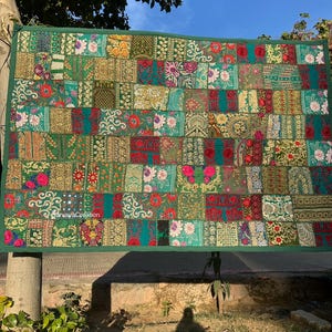 May include: A large green patchwork tapestry with colorful embroidery and floral patterns. The tapestry is made of different fabrics and textures, creating a unique and eclectic look.