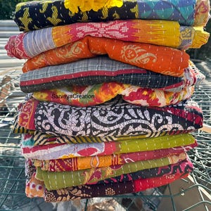 Peut inclure: Une pile de courtepointes kantha colorées avec différents motifs et designs. Les courtepointes sont faites de saris recyclés et sont cousues à la main. Les courtepointes sont disposées en pile sur une surface métallique. Le texte "SarvayaCreation" est visible sur l'une des courtepointes.