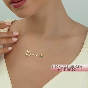 May include: Gold necklace with a cursive name "Brianna" and a small green gemstone. The necklace is available in lengths of 14", 16", 18", and 20".