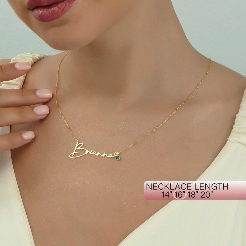 May include: Gold necklace with a cursive name "Brianna" and a small green gemstone. The necklace is available in lengths of 14", 16", 18", and 20".