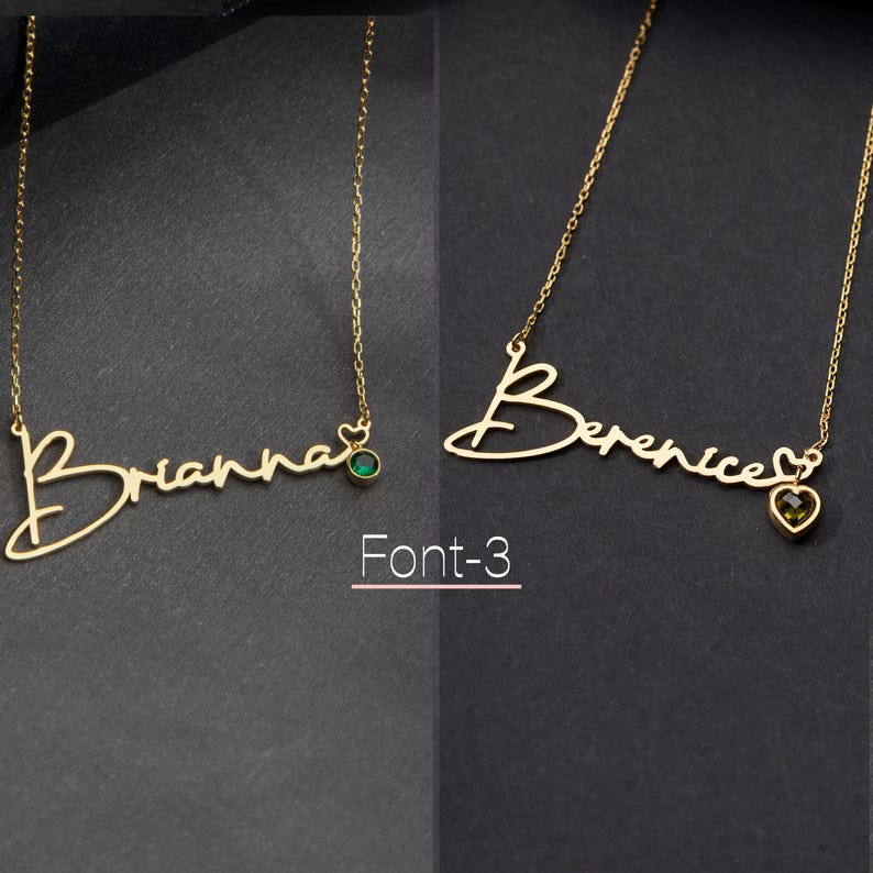 May include: Two gold necklaces with a cursive name and a small gemstone pendant. The necklace on the left says "Brianna" with a green gemstone. The necklace on the right says "Berenice" with a brown gemstone. The text "Font-3" is below the necklaces.