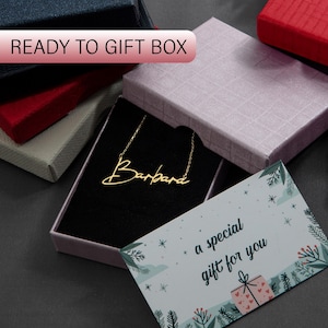 May include: A gold necklace with the name "Barbara" written in cursive script, inside a purple gift box with a black velvet interior. A small card with the text "a special gift for you" is next to the box.