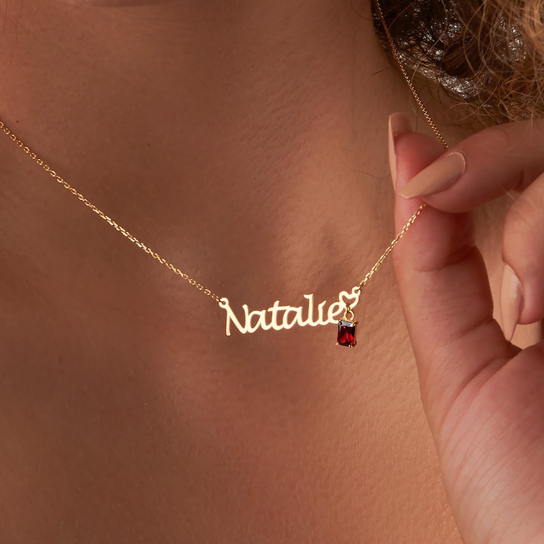 May include: A gold necklace with a cursive nameplate that reads "Natalie" and a small red gemstone pendant.