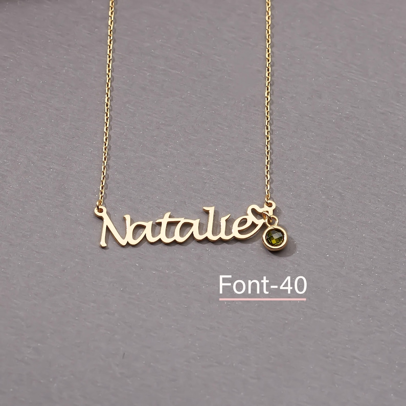 May include: Gold necklace with the name "Natalie" in a cursive font and a small green gemstone pendant. The text "Font-40" is below the necklace.