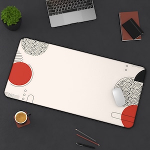 Könnte beinhalten: Eine weiße Schreibtischunterlage mit einem geometrischen Design in Schwarz und Rot. Das Design zeigt Kreise, Wellen und Linien. Die Unterlage liegt auf einer schwarzen Oberfläche mit einem Laptop, einer Tasse Kaffee und Bleistiften.