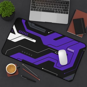 Könnte beinhalten: Ein rechteckiges, schwarz-violettes Mauspad mit einer weißen Maus. Das Pad hat ein geometrisches Design mit weißen und violetten Linien und Formen. Ein Laptop, eine Kaffeetasse und Schreibwaren sind ebenfalls zu sehen.