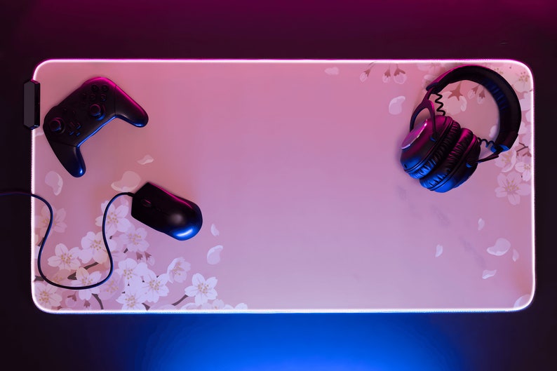 May include: A pink gaming mouse pad with a floral design, a black wireless mouse, a black video game controller, and black over-ear headphones.