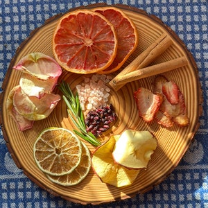 May include: A wooden platter with a variety of dried fruits, including grapefruit, apple, and strawberry slices. There are also cinnamon sticks, pink Himalayan salt, and rosemary sprigs on the platter.