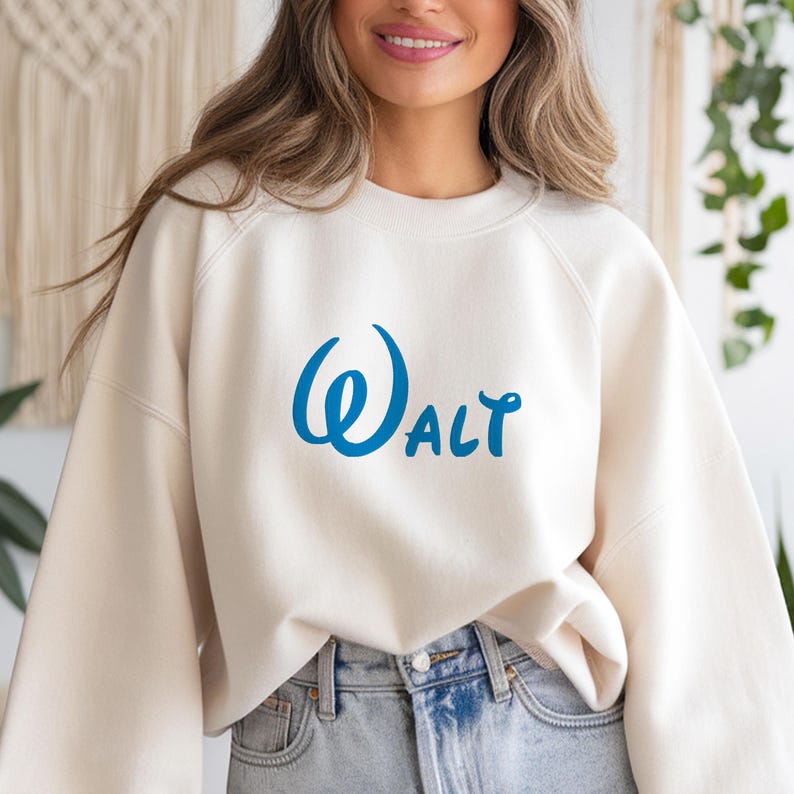 May include: Cream-colored sweatshirt with the word "Walt" in blue script. The sweatshirt has a crew neck and long sleeves. The text is in a stylized font.