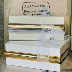 May include: White gift boxes stacked with silver and gold metallic detailing. A white lace ribbon and bow with a gold accent decorates the boxes. The text "Add Your Own Personalisation" is in a speech bubble.