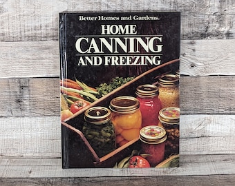 May include: A vintage cookbook titled "Home Canning and Freezing" by Better Homes and Gardens. The cover features a dark background with the title in white lettering. The image includes jars filled with colorful preserved foods, such as tomatoes, beans, and corn.