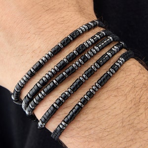 Könnte beinhalten: Ein mehrreihiges Armband aus schwarzen und silbernen Perlen. Das Armband besteht aus kleinen, runden Perlen, die auf einer Schnur aufgefädelt sind.