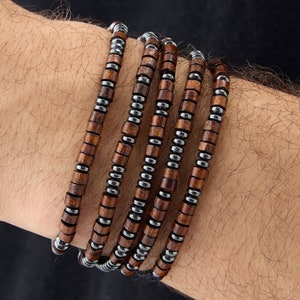 Peut inclure: Un bracelet composé de perles en bois brun et de perles en métal argenté. Le bracelet est superposé et enroulé autour d'un poignet.