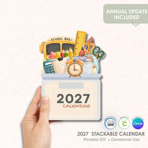 May include: A 2027 stackable calendar with a school theme. The calendar is held by a hand and features a school bus, pencils, scissors, and an alarm clock. The text "2027 CALENDAR" is displayed prominently.