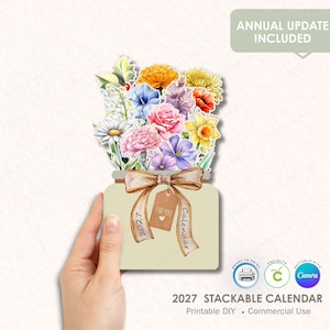 Puede incluir: Un calendario apilable de 2027 con un diseño de ramo de flores. El calendario tiene forma de tarro con una cinta y una etiqueta que dice "Para ti". El texto "Actualización anual incluida" está en la parte superior. El texto inferior dice "Calendario apilable 2027".