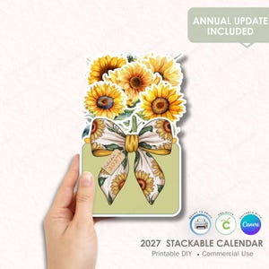 Puede incluir: Una pegatina decorativa con un ramo de girasoles, un lazo con diseños de girasoles y el texto "Calendario 2027". La pegatina está etiquetada como "Actualización anual incluida" y "Calendario apilable 2027".