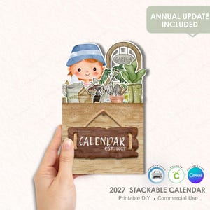 Puede incluir: Un calendario apilable de 2027 estilo acuarela con temática de jardinería. El diseño presenta un personaje de dibujos animados con un sombrero azul, herramientas de jardinería y la palabra "CALENDAR" en un letrero de madera. También se ve el texto "ANNUAL UPDATE INCLUDED".