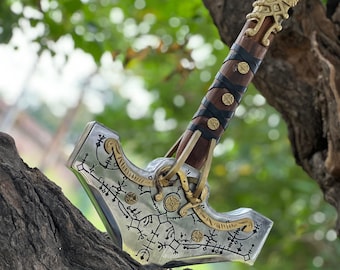 May include: A detailed, metallic hammer with intricate engravings and gold accents. The handle is wrapped in dark leather and adorned with gold studs. The hammer is set against a blurred green and brown background.