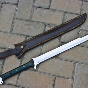May include: A long, silver blade sword with a dark green handle and a brown leather sheath. The sheath is stitched with yellow thread and has a strap with a gold button. The sword is lying on a brick surface.