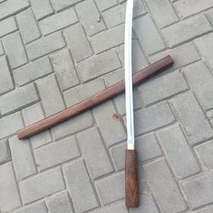 May include: A Japanese-style sword with a curved, silver blade and a dark wood handle. The sword is partially unsheathed from its matching wooden scabbard. The handle and scabbard have a rich, dark brown color, suggesting a natural wood grain.