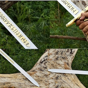 May include: A silver sword with a gold hilt and a brown leather-wrapped handle. The blade has etched gold lettering. The sword is displayed against a backdrop of green foliage and a tree trunk.
