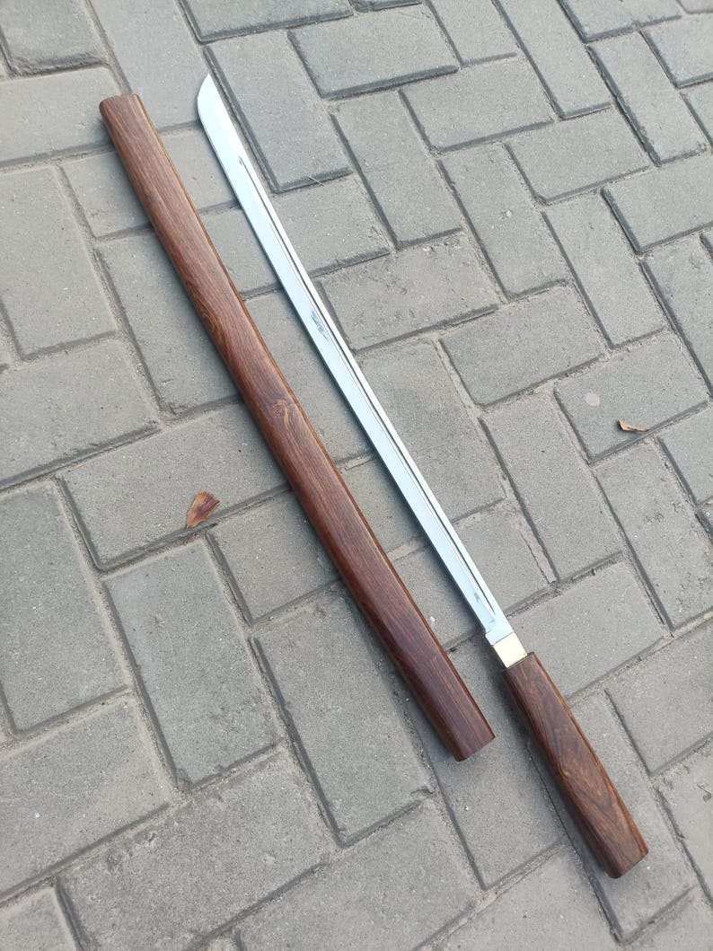 May include: A Japanese-style sword with a polished steel blade and a dark brown wooden scabbard and handle. The blade is straight with a slight curve at the tip. The scabbard is a dark, rich brown color. The handle is also dark brown with a brass accent.