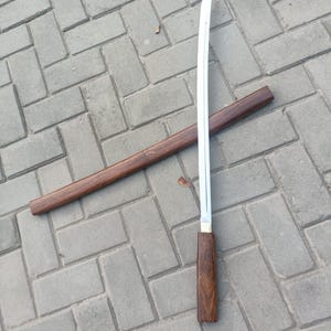 May include: A Japanese-style sword with a polished steel blade and a wooden handle. The sword is partially sheathed in a matching wooden scabbard. The handle and scabbard are a dark brown color.