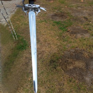 May include: A long, silver sword with a decorative hilt and a black handle. The blade is highly polished, reflecting the surrounding environment. The sword is held against a backdrop of green grass.