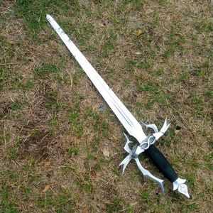 May include: A silver-colored sword with a black handle lies on a bed of grass. The sword has a long, pointed blade and an ornate hilt with decorative elements. The handle appears to be wrapped in black material.