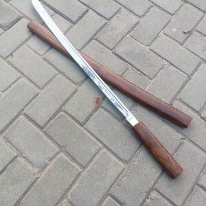 May include: A Japanese-style sword with a polished steel blade and a dark wood handle. The sword is partially unsheathed from its matching wooden scabbard. The handle and scabbard have a rich, dark brown color.