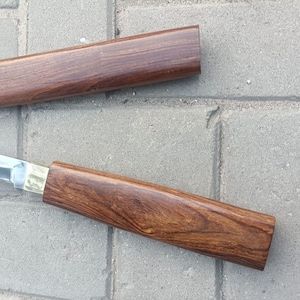 May include: A close-up of a sword with a polished steel blade and a wooden handle. The handle is a rich brown color with a brass accent. The scabbard is also made of wood, matching the handle's color.