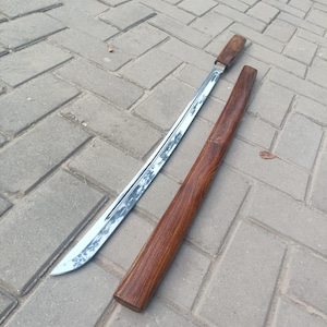 May include: A traditional sword with a polished steel blade and a wooden handle, resting beside its matching wooden scabbard. The blade has a curved edge. The scabbard and handle are a rich, dark brown color.